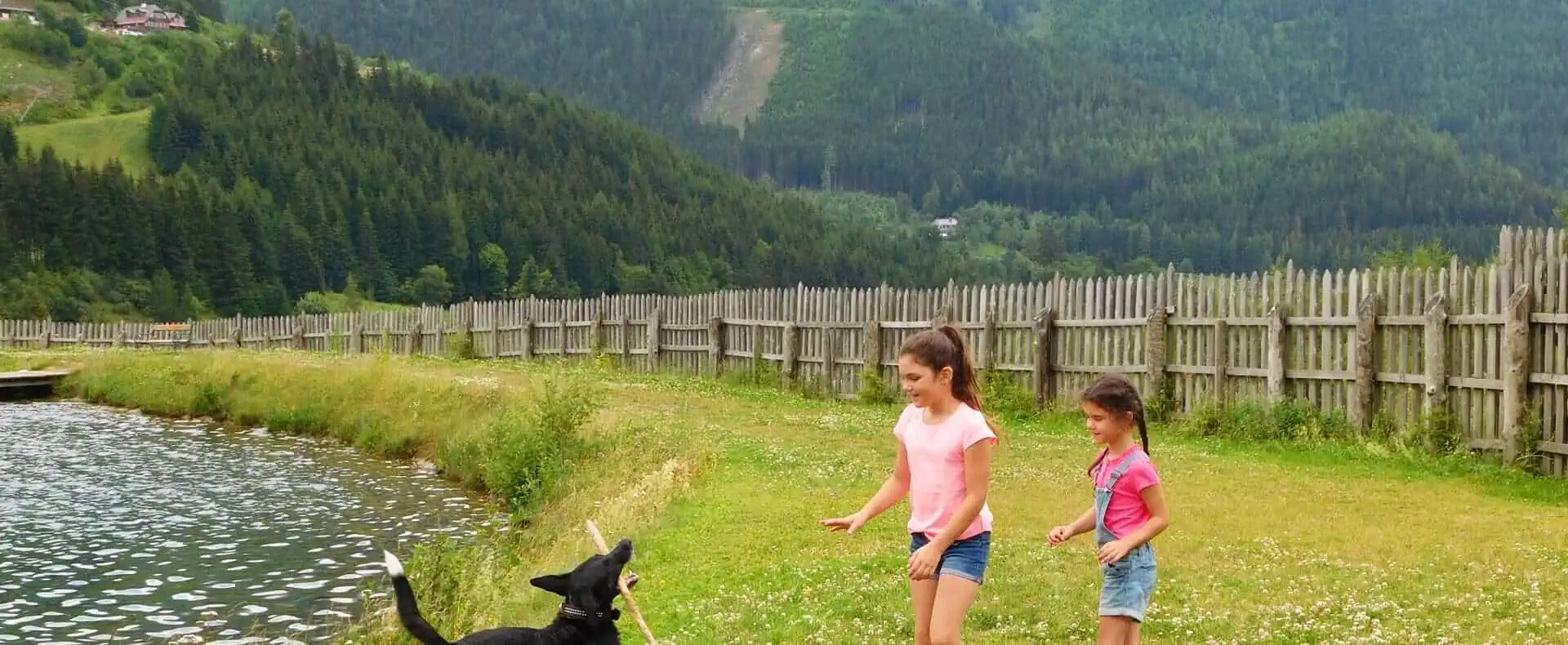 Hund spielt am Teich mit zwei Kindern