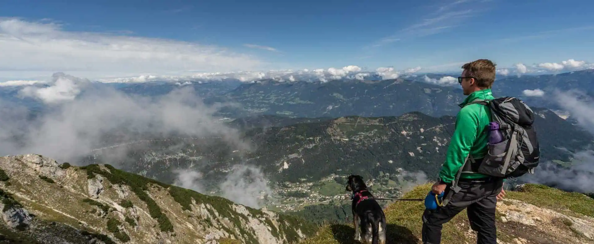 Ein Wanderer und sein Hund genießen den Ausblick auf die Berge beim Wandern. (c)Carolin Thiersch