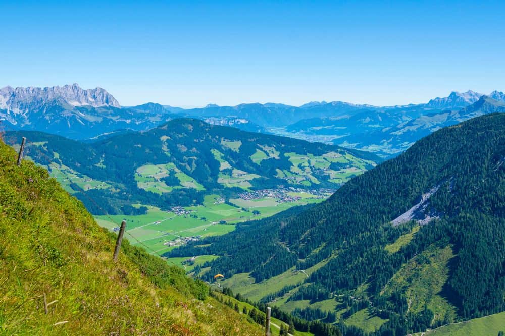 Ein Panoramablick auf ein weites grünes Tal, durchsetzt mit Dörfern, umgeben von üppigen bewaldeten Hügeln und hohen Bergen.