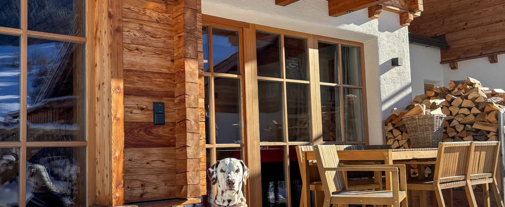 Dalmatiner vor einem hundefreundlichen Chalet im Winter mit Holzterrasse, Schnee und gemütlichem Sitzbereich.