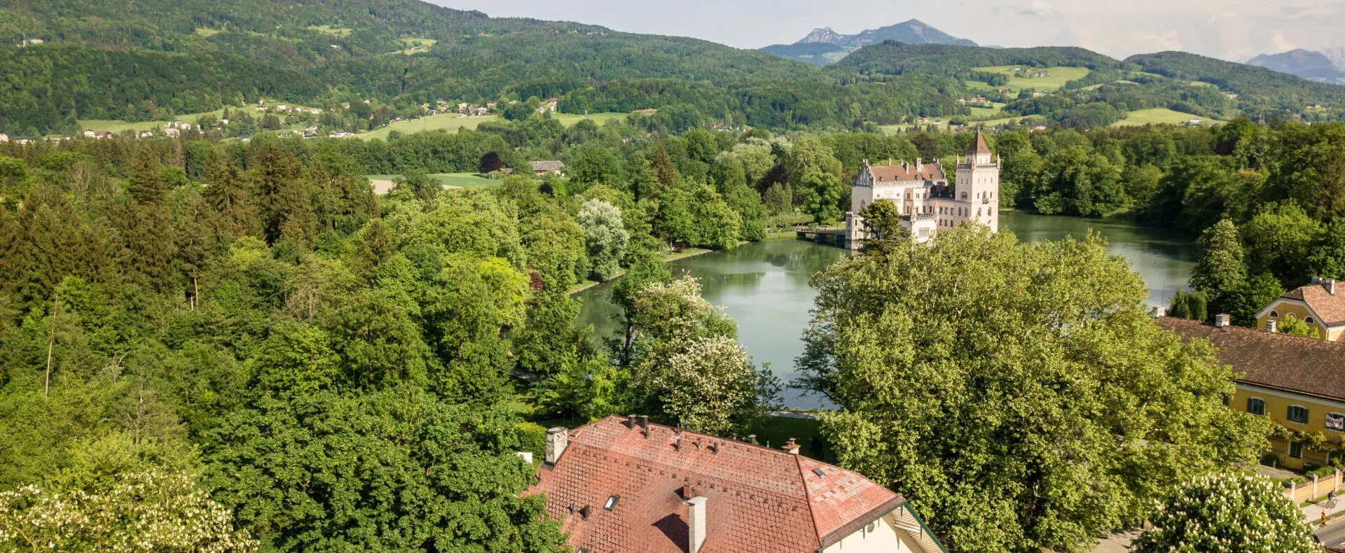 Luftaufnahme vom Hotel Schlosswirt zu Anif mit Blick auf Schloss Anif, See und grüne Landschaft.