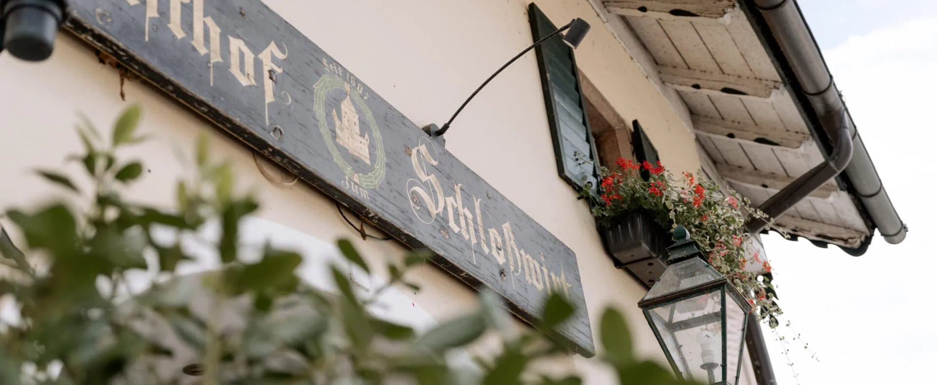 Historisches Schild am Eingang des Schlosswirt zu Anif mit Laterne und Blumenschmuck.