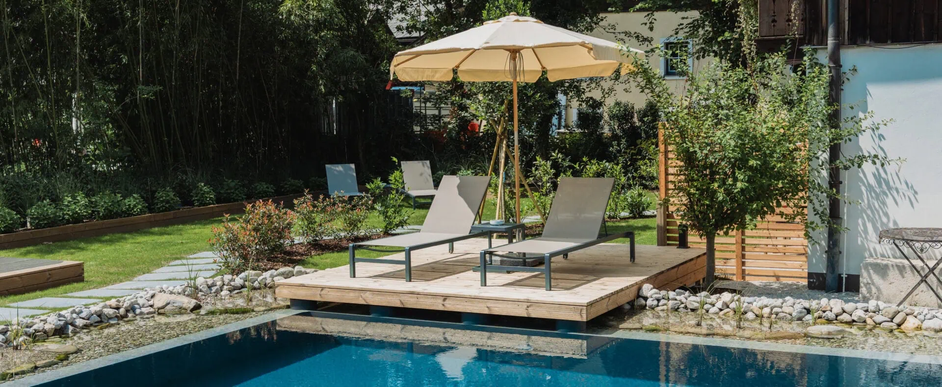 Naturpool im Garten des Schlosswirt zu Anif mit Liegen, Sonnenschirm und ruhiger Atmosphäre.