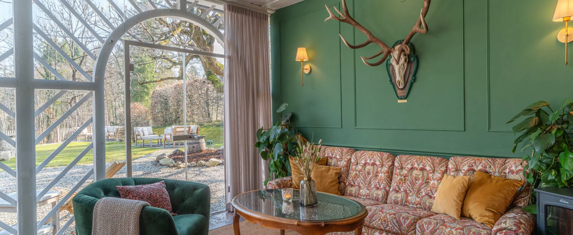Stilvolle Salettl-Lounge im Schlosswirt zu Anif mit grüner Wand, Sofa und Blick in den Garten.