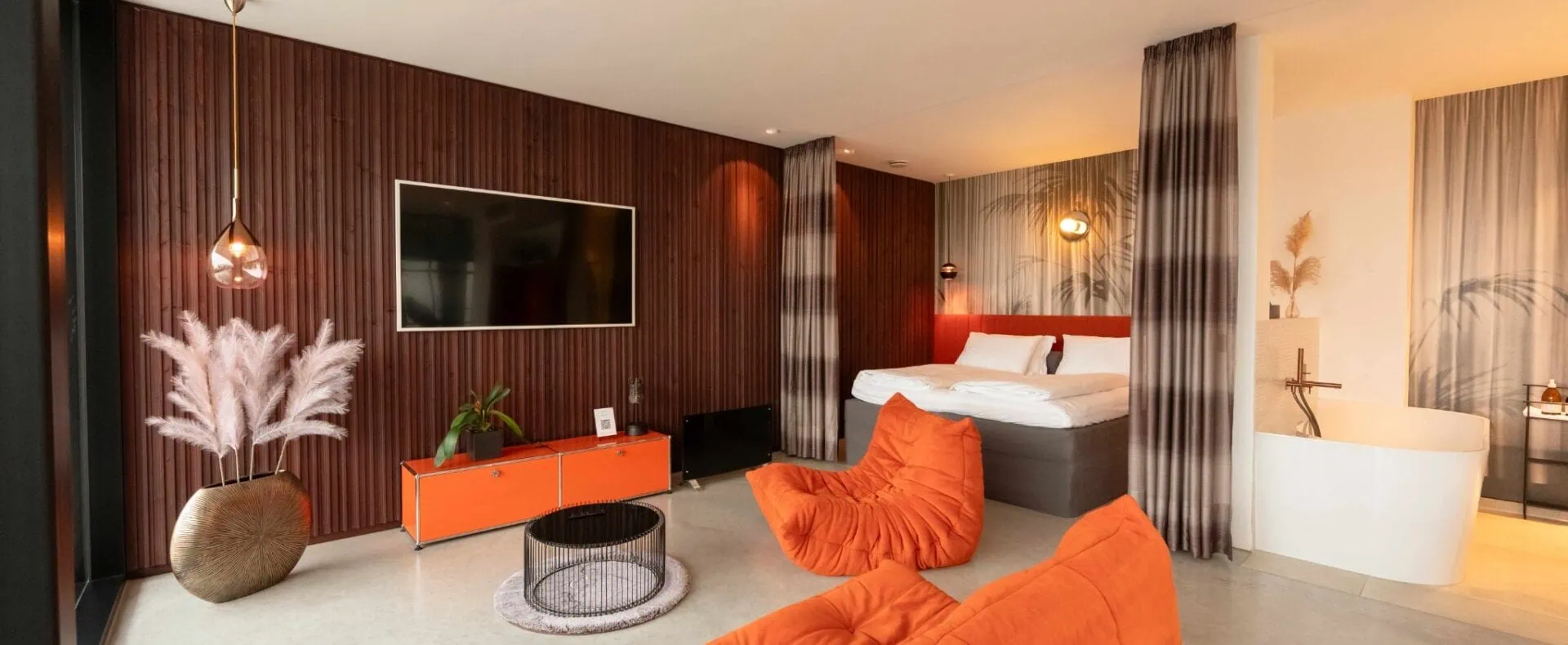 Großzügiges Design-Apartment der ORANGE LOUNGE am Attersee mit Doppelbett, orangefarbenen Sitzmöbeln und freistehender Badewanne.