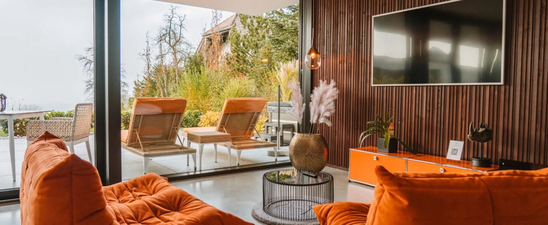 Moderner Wohnbereich der ORANGE LOUNGE am Attersee mit orangefarbenen Sitzmöbeln und Blick auf die Terrasse mit Liegestühlen.